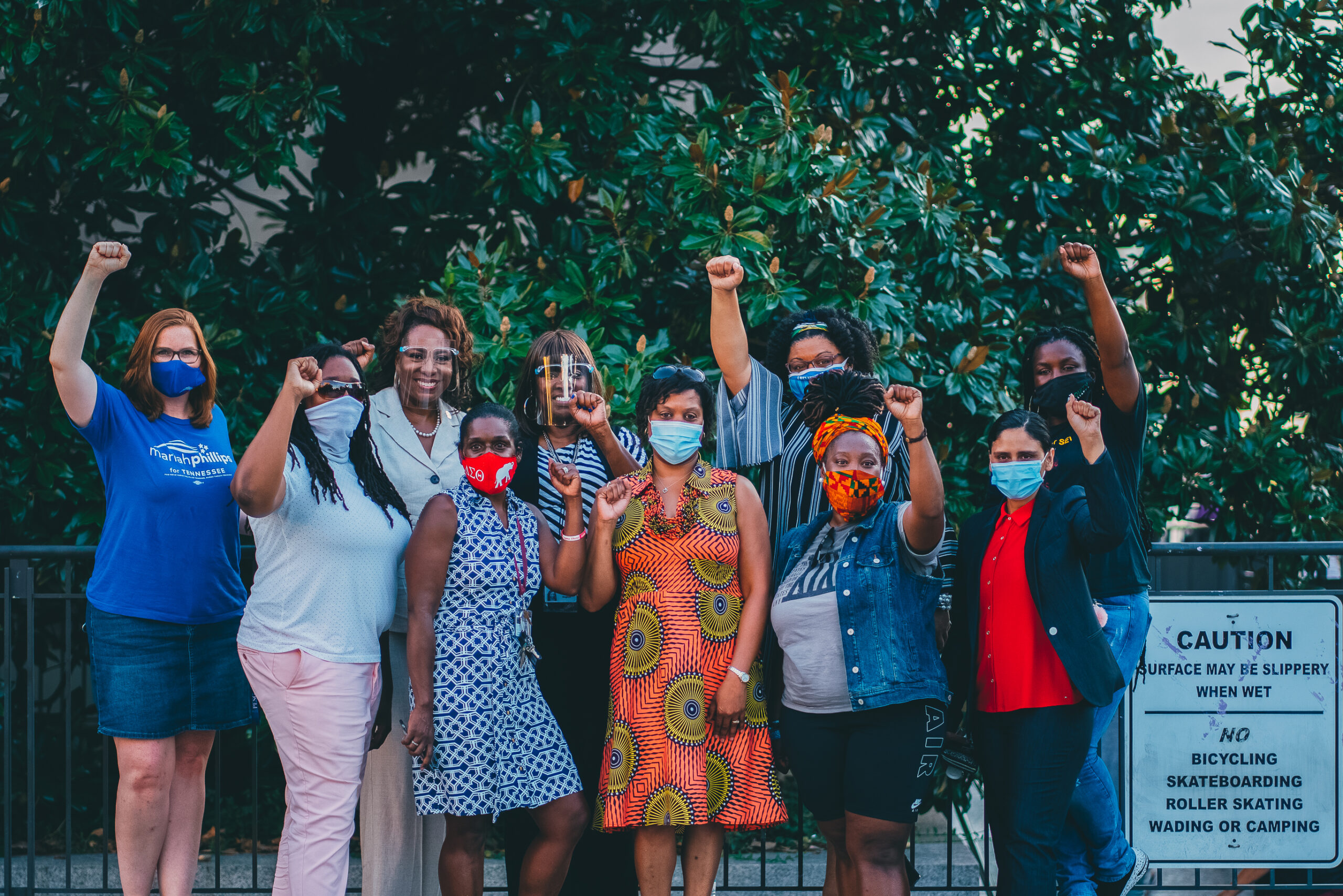 A group of people standing together, masked, some with fists in the air.